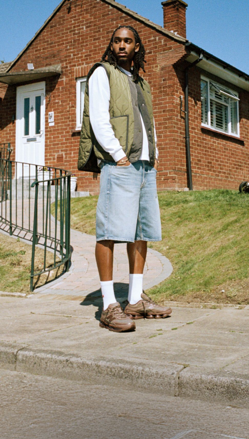 Djed Spence standing in front of a brick house wearing brown New Balance sneakers.
